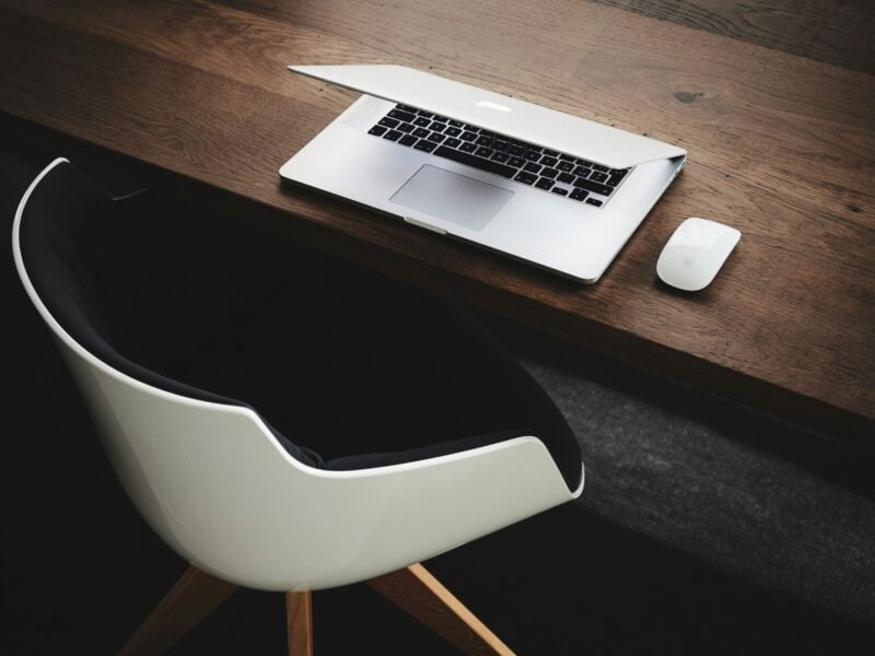 Laptop and wireless mouse on a wooden desk beside a white office chair