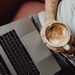 Person working on a laptop with coffee, related to Estonia company formation costs.